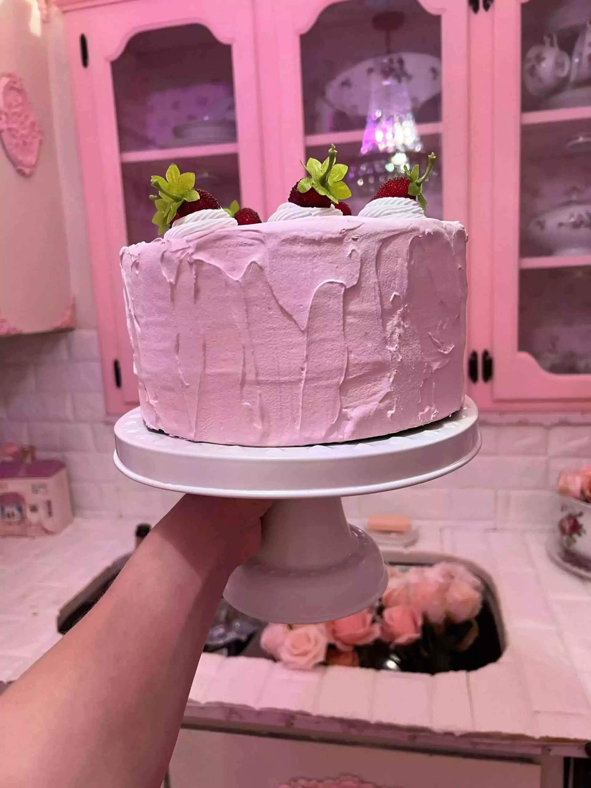Katie holding pink cake on stand in kitchen