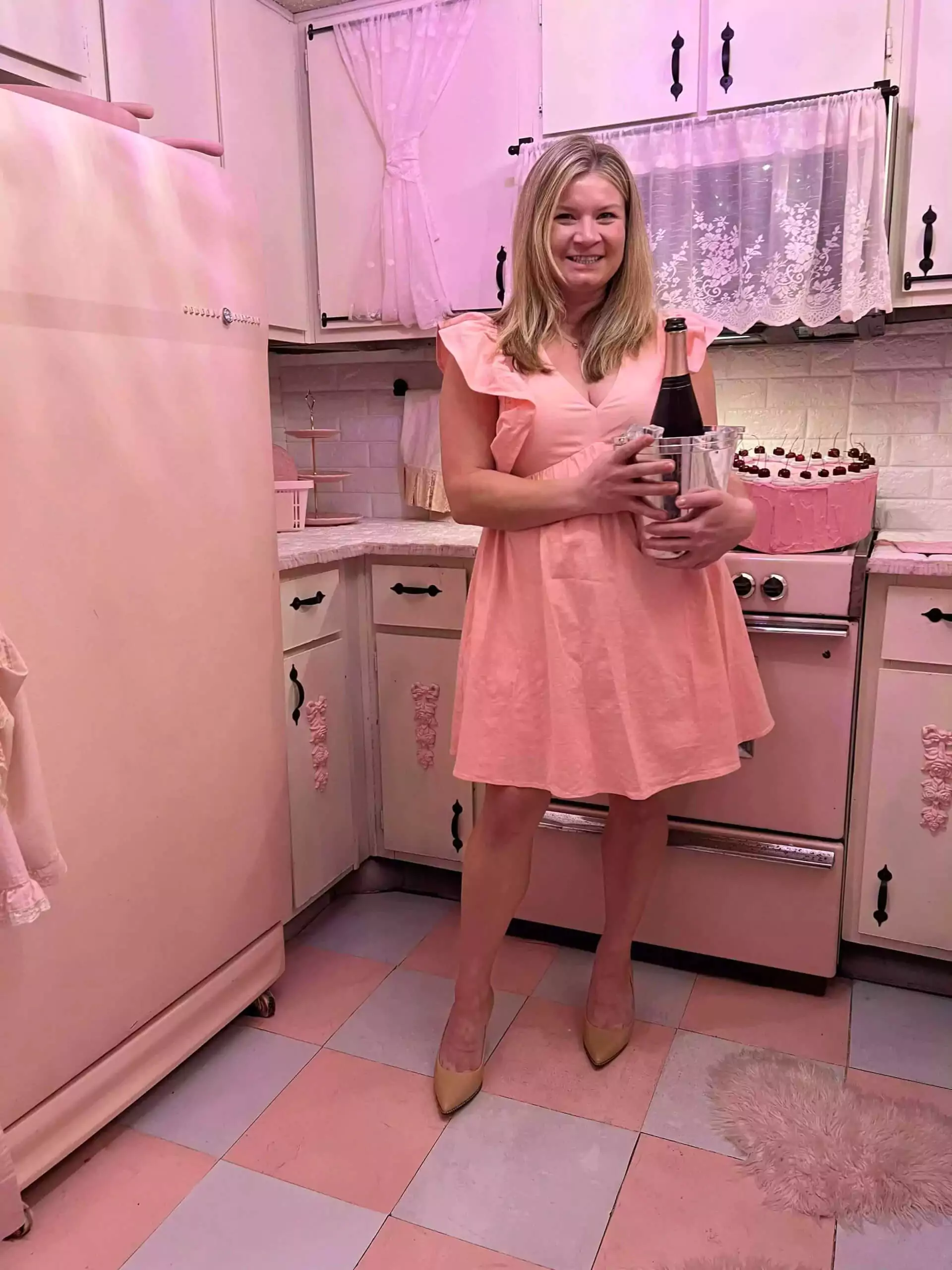 Katie wearing pink dress holding champagne bucket in kitchen